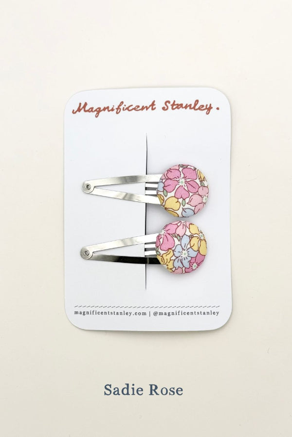 Pair of liberty sadie rose floral hair clips on a 'Magnificent Stanley' branded card.