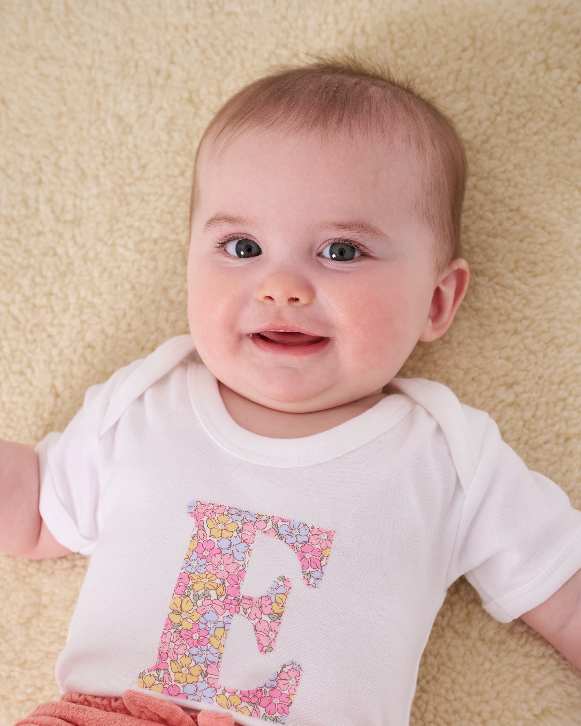 a 6 month old baby wearing a personalised bodysuit baby grow with her initial cut from floral sadie rose Liberty print