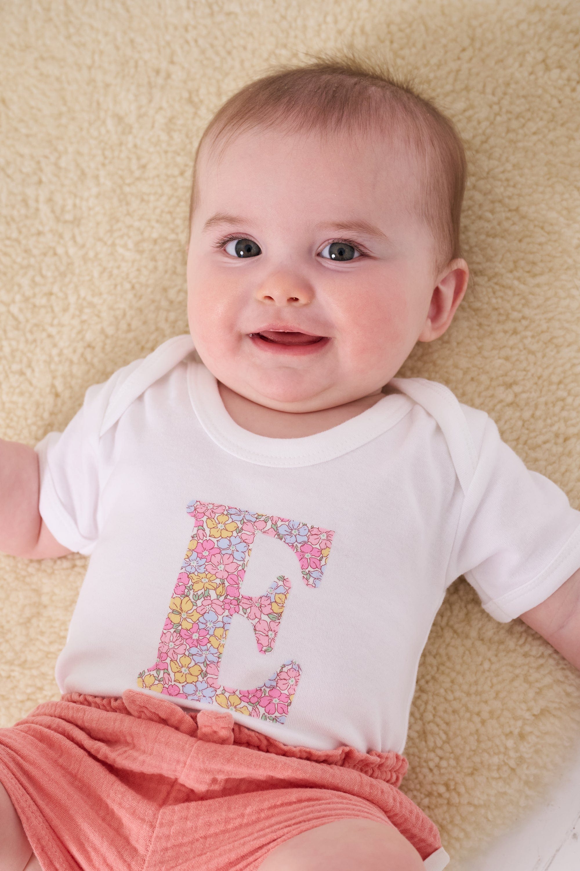 a 6 month old baby wearing a personalised bodysuit baby grow with her initial cut from floral sadie rose Liberty print