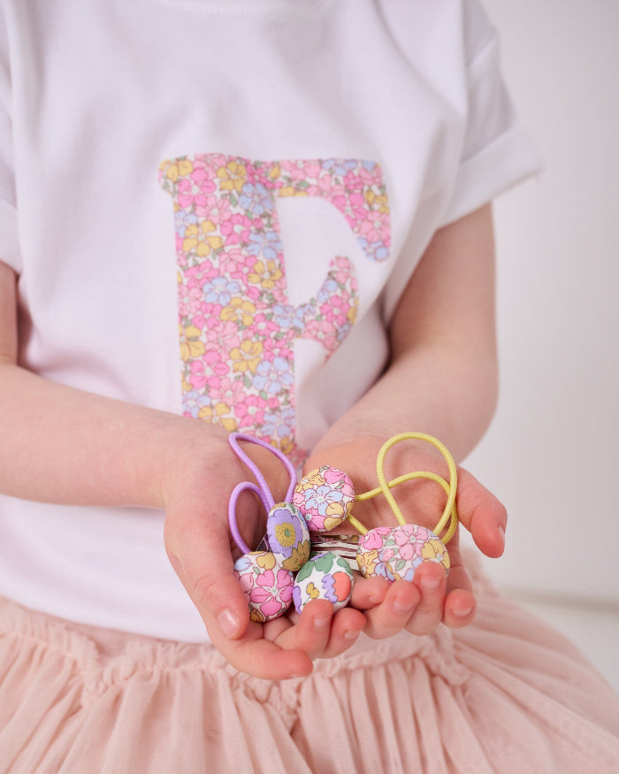 a little girl's hands holding liberty print hair clips and hair bobble elastics