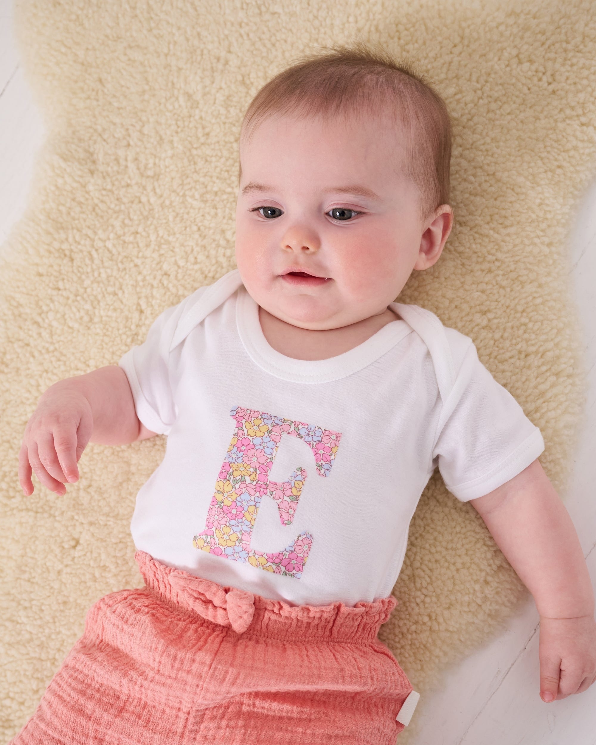 a 6 month old baby wearing a personalised bodysuit baby grow with her initial cut from floral sadie rose Liberty print