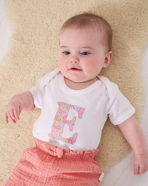 a 6 month old baby wearing a personalised bodysuit baby grow with her initial cut from floral sadie rose Liberty print