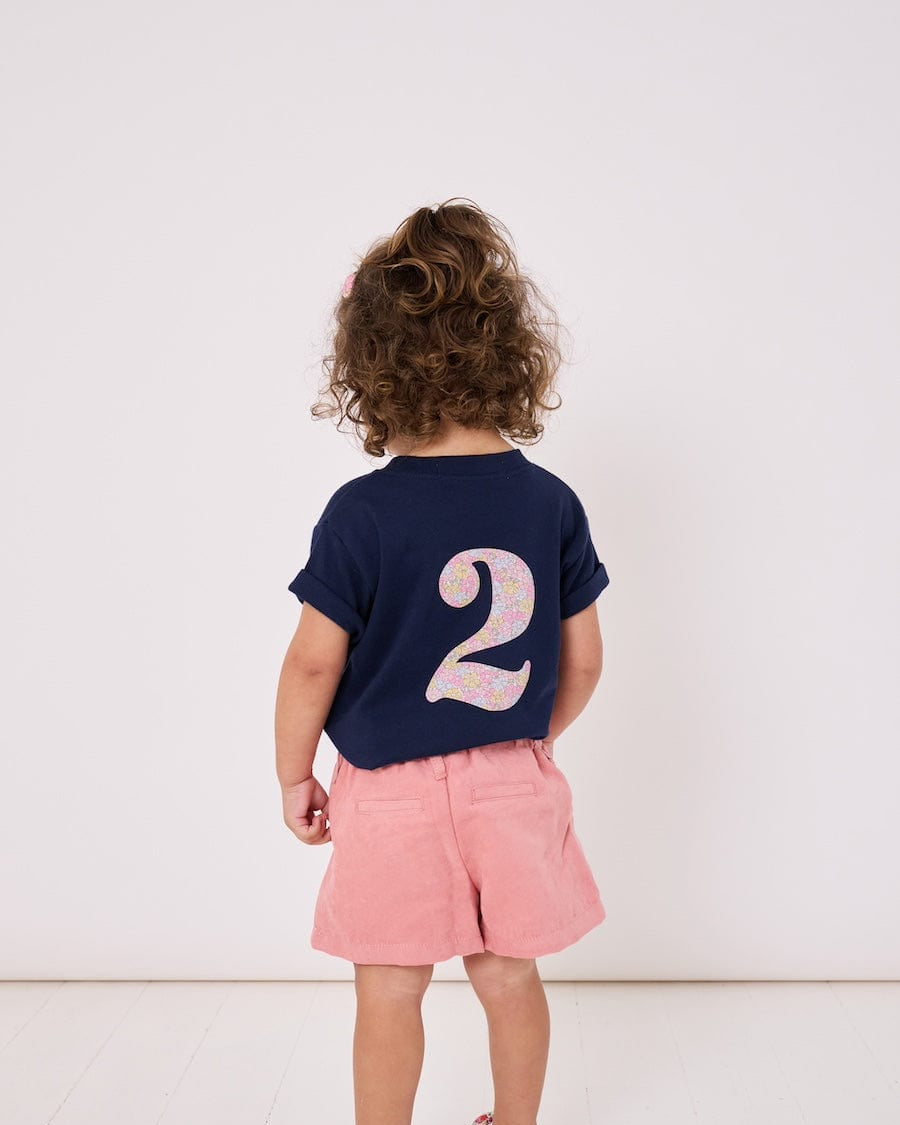 A 2 year old girl wearing a kids cotton t-shirt with a Liberty print number 2 on the back.