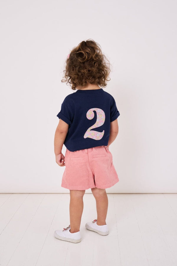 A 2 year old girl wearing a kids cotton t-shirt with a Liberty print number 2 on the back.