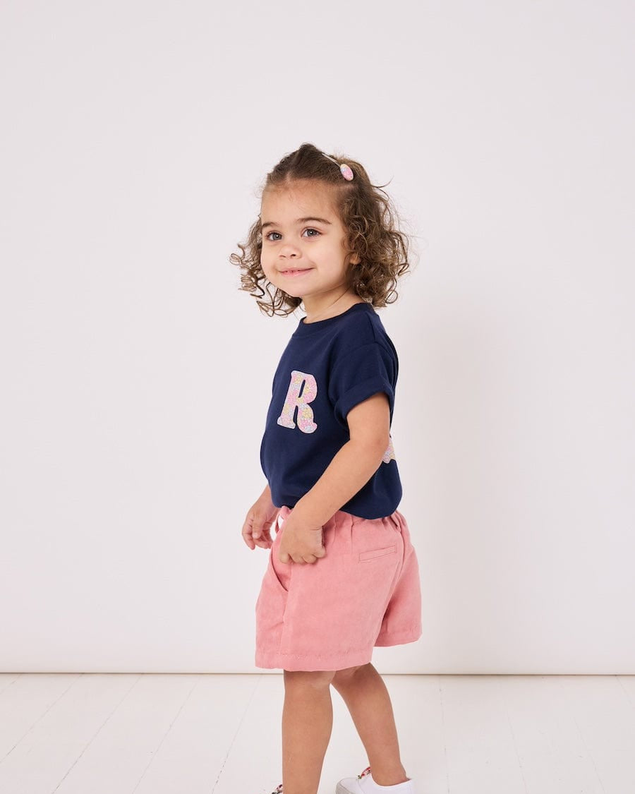 A smiling 2 year old girl wearing a personalised kids cotton t-shirt with a Liberty print initial on the front.