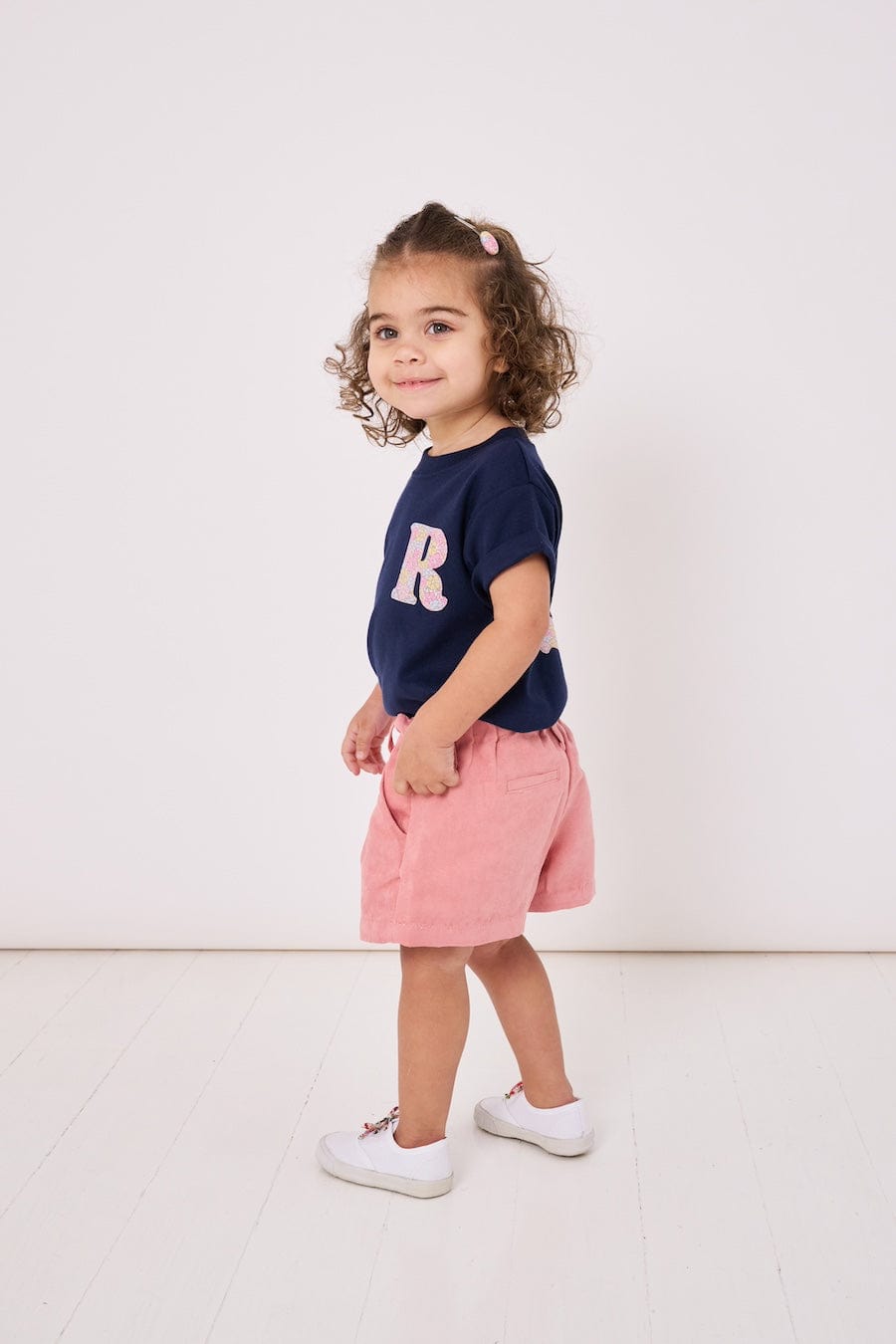 A smiling 2 year old girl wearing a personalised kids cotton t-shirt with a Liberty print initial on the front.