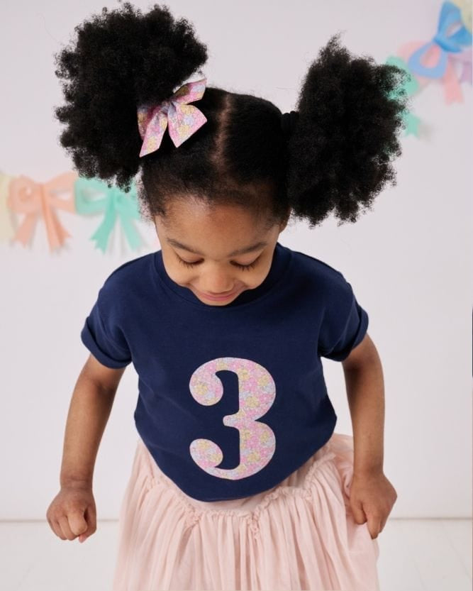 a 3 year old girl wearing a magnificent stanley navy birthday t-shirt with a number 3 cut from sadie rose floral liberty print on the front