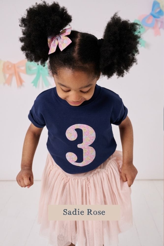 a 3 year old girl wearing a magnificent stanley navy birthday t-shirt with a number 3 cut from sadie rose floral liberty print on the front