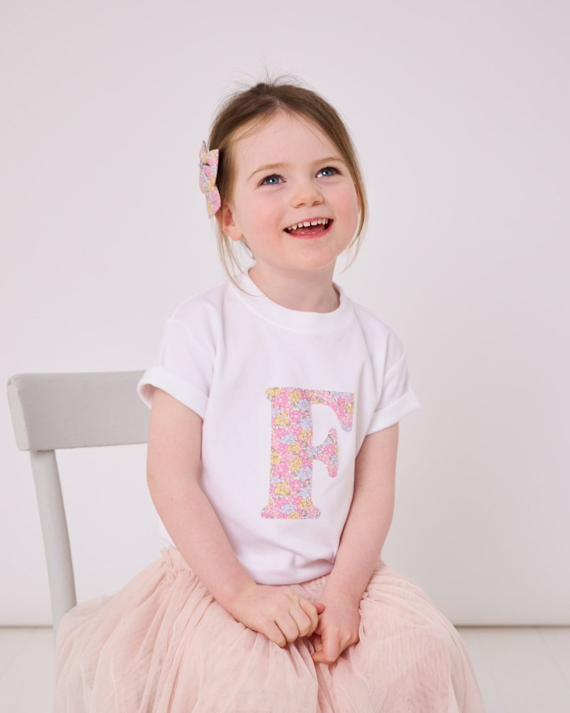 a little girl wearing a personalised kids white cotton t-shirt with an initial cut from sadie rose liberty floral print on the front