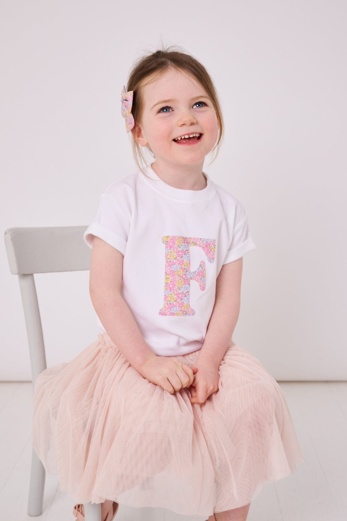 a little girl wearing a personalised kids white cotton t-shirt with an initial cut from sadie rose liberty floral print on the front