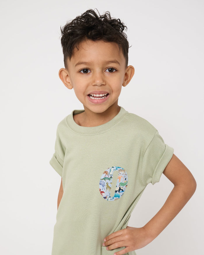 a 4 year old boy wearing a sage green t-shirt with a small initial on the front cut from zoo animal Liberty print