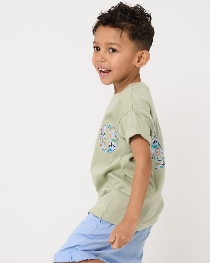 a 4 year old boy wearing a sage green t-shirt with a small initial on the front cut from zoo animal Liberty print