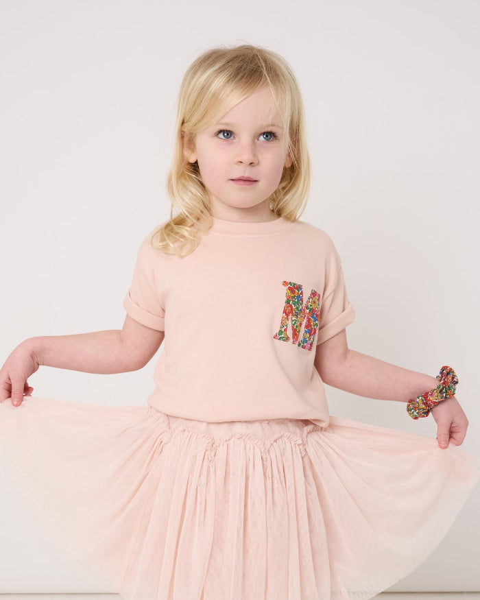A 4 year old girl wearing a pale pink t-shirt with a Liberty Nell Annie and May floral small initial on the front
