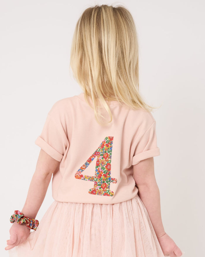 A 4 year old girl wearing a pale pink t-shirt with a Liberty Nell Annie and May floral small initial on the front