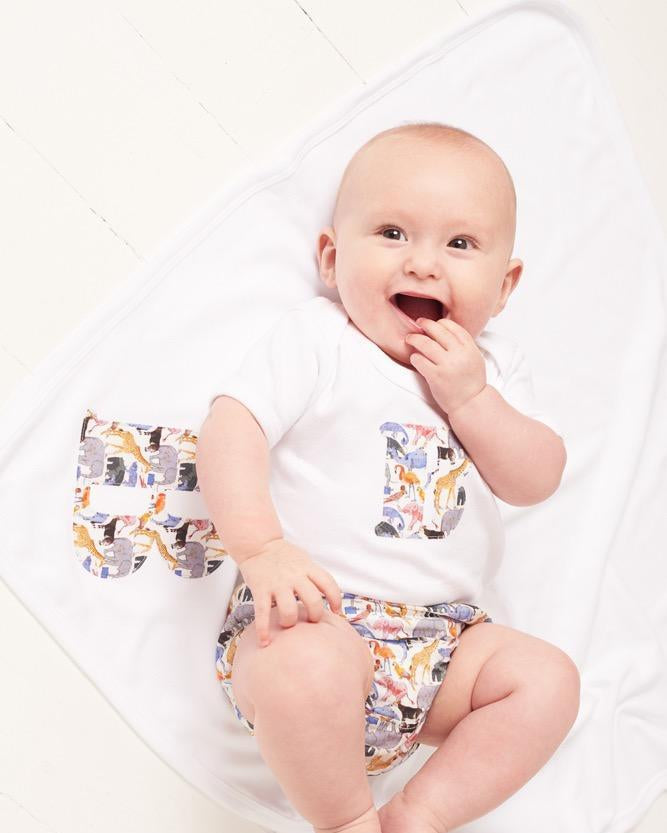 A newborn baby laying on Personalised Liberty Print Cotton Baby Blanket with their initial sewn on it.