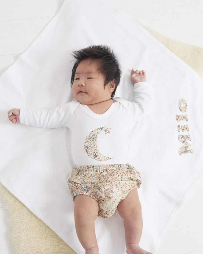 A new baby in a white cotton babygrow with a moon and hanging star sewn on the front, cut from Adelajda starry Liberty print.