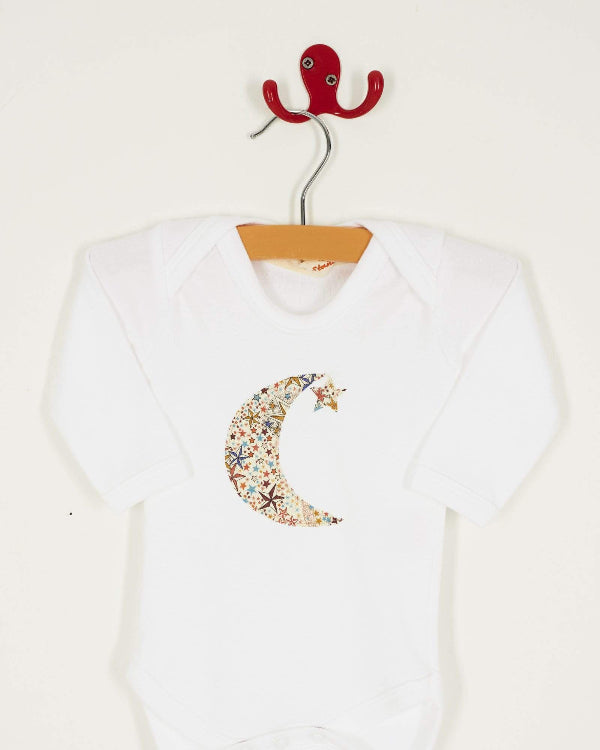 A white cotton babygrow with a moon and hanging star sewn on the front, cut from Adelajda starry Liberty print.