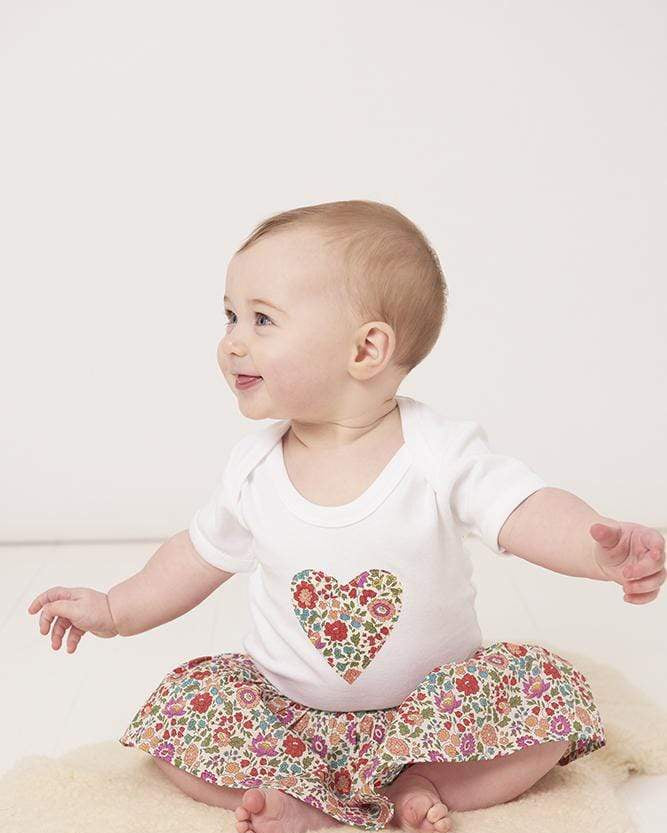 a smiling baby wearing a bodysuit with a heart on made from d'anjo liberty print fabric