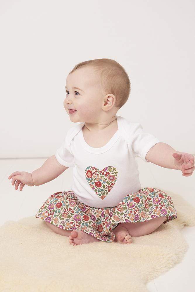 a smiling baby wearing a bodysuit with a heart on made from d'anjo liberty print fabric