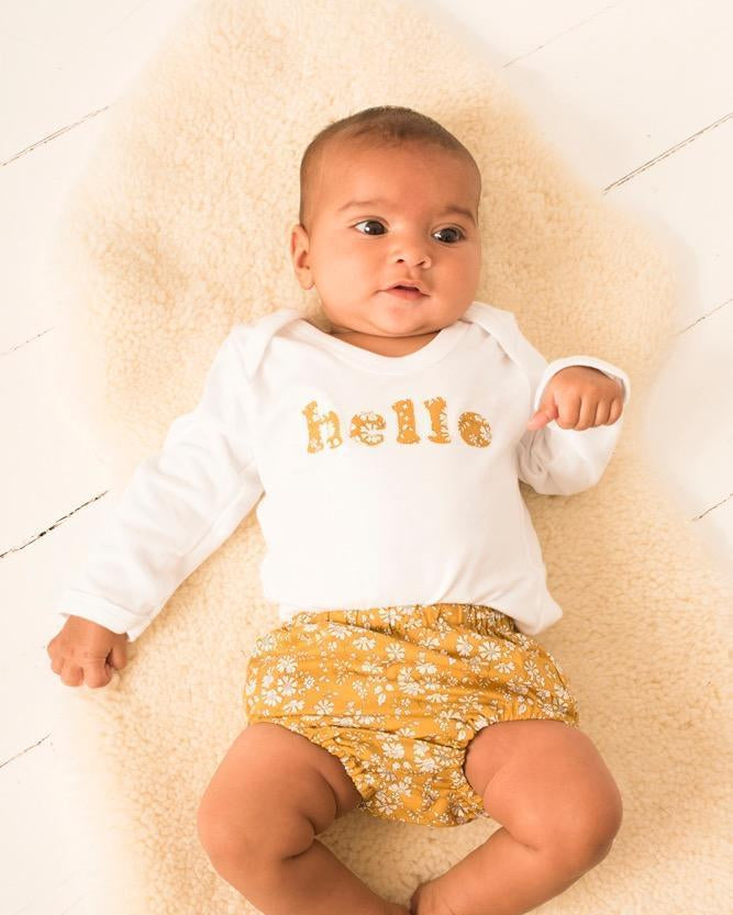 Magnificent Stanley Bodysuit 'hello' Bodysuit in choice of Liberty Print Magnificent Stanley Bodysuit 'hello' Bodysuit. New baby wears a white bodysuit with the word hello on it. the letters are cut from a mustard capel floral liberty print