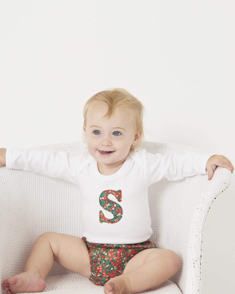 A smiling baby wearing a personalised initial Magnificent Stanley baby Bodysuit in Glitter Wiltshire Liberty Print