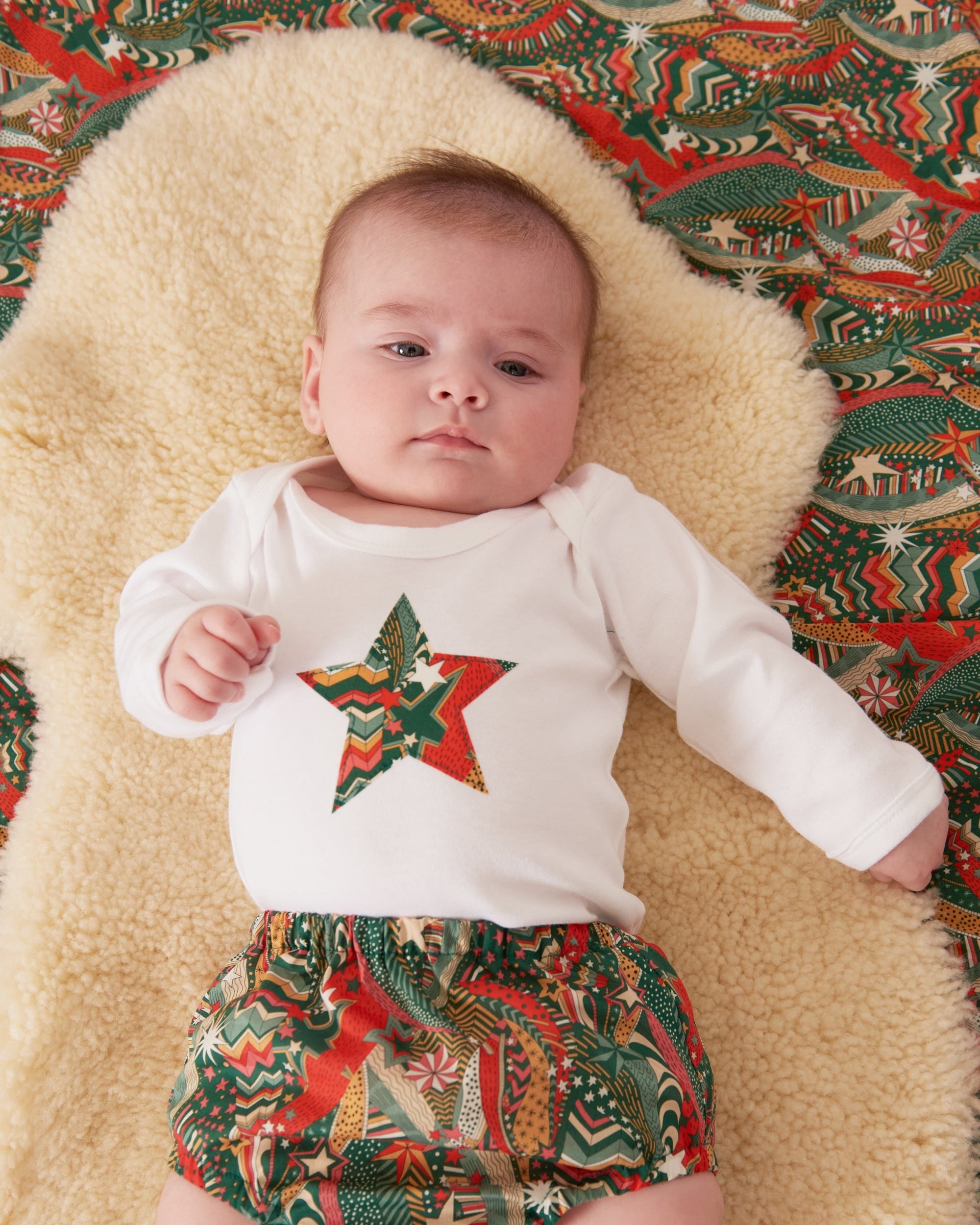 A baby wearing a white bodysuit babygrow with a Liberty My Little Star print festive star sewn on the front.