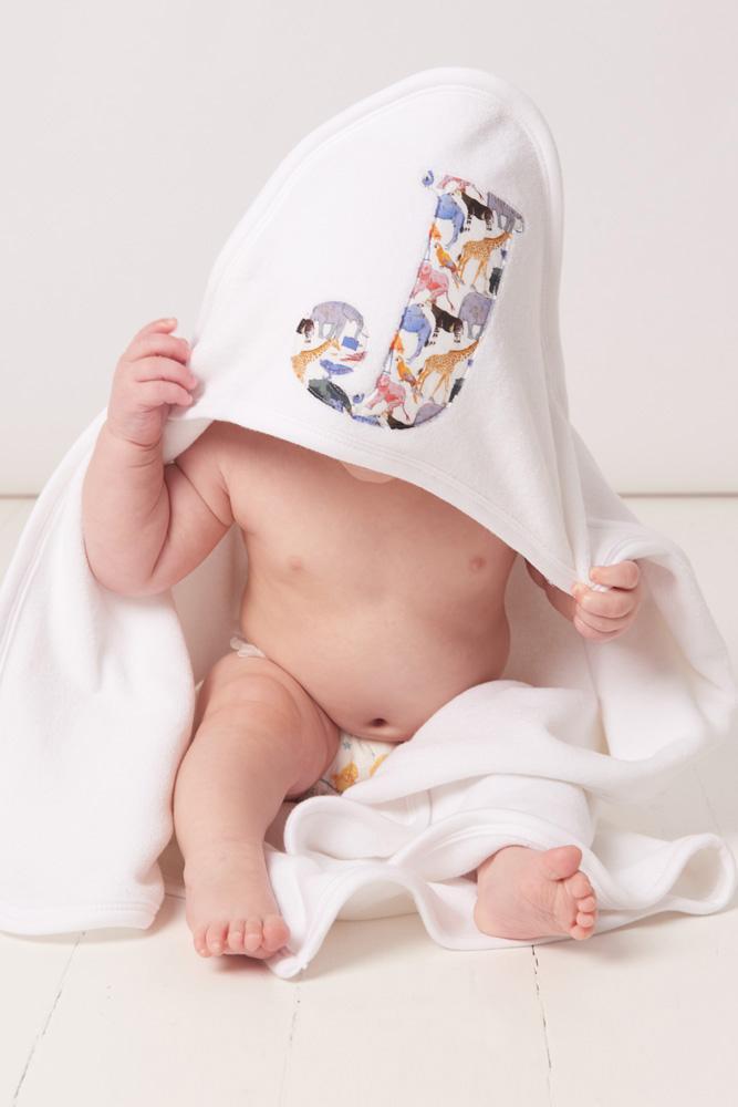 A little baby wearing a soft cotton hooded baby towel with his initial sewn on the hood in queue for the zoo liberty print