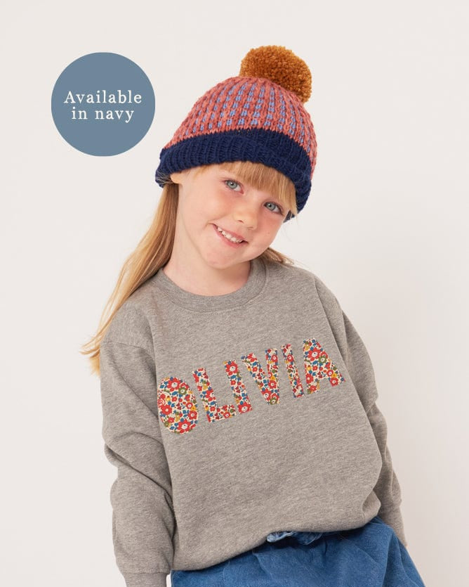a smiling 5 year old girl wearing a grey kids personalised sweatshirt with her name on it cut from Betsy Ann Liberty print.