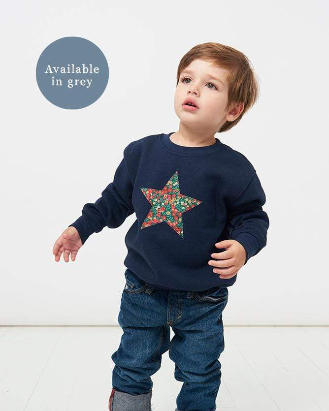 A little boy wearing a Christmas star jumper navy sweatshirt with a liberty Wiltshire star on the front