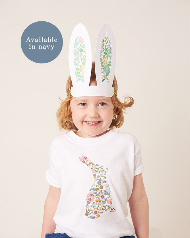 A smiling girl wearing a white cotton t-shirt with a floral liberty print bunny on the front and she has liberty betsy bunny ears on her head.