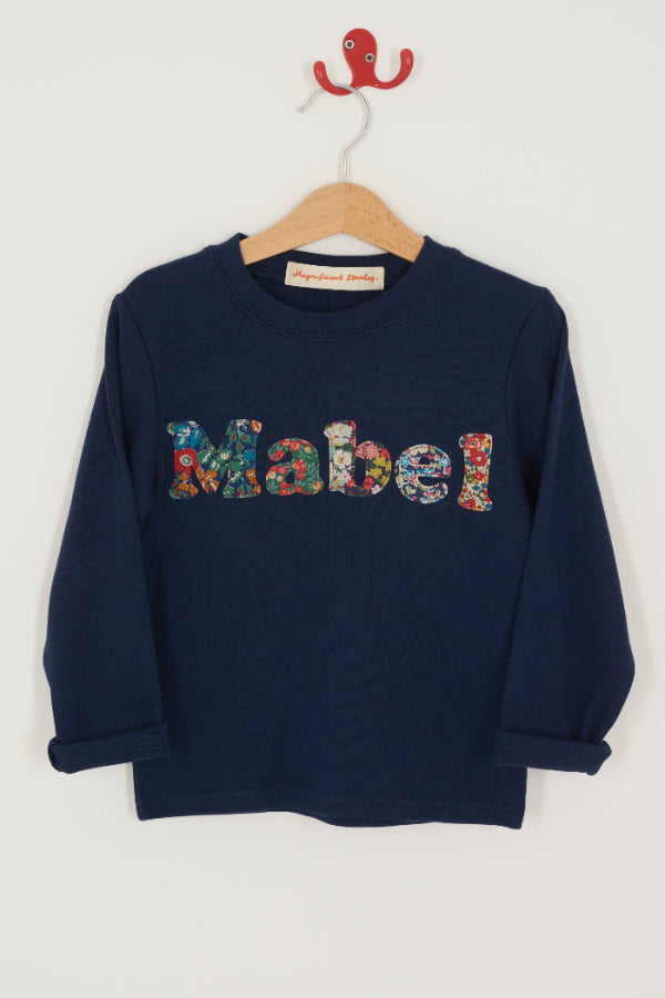 A navy t-shirt with the name mabel sewn on in mixed Liberty print lowercase letters.