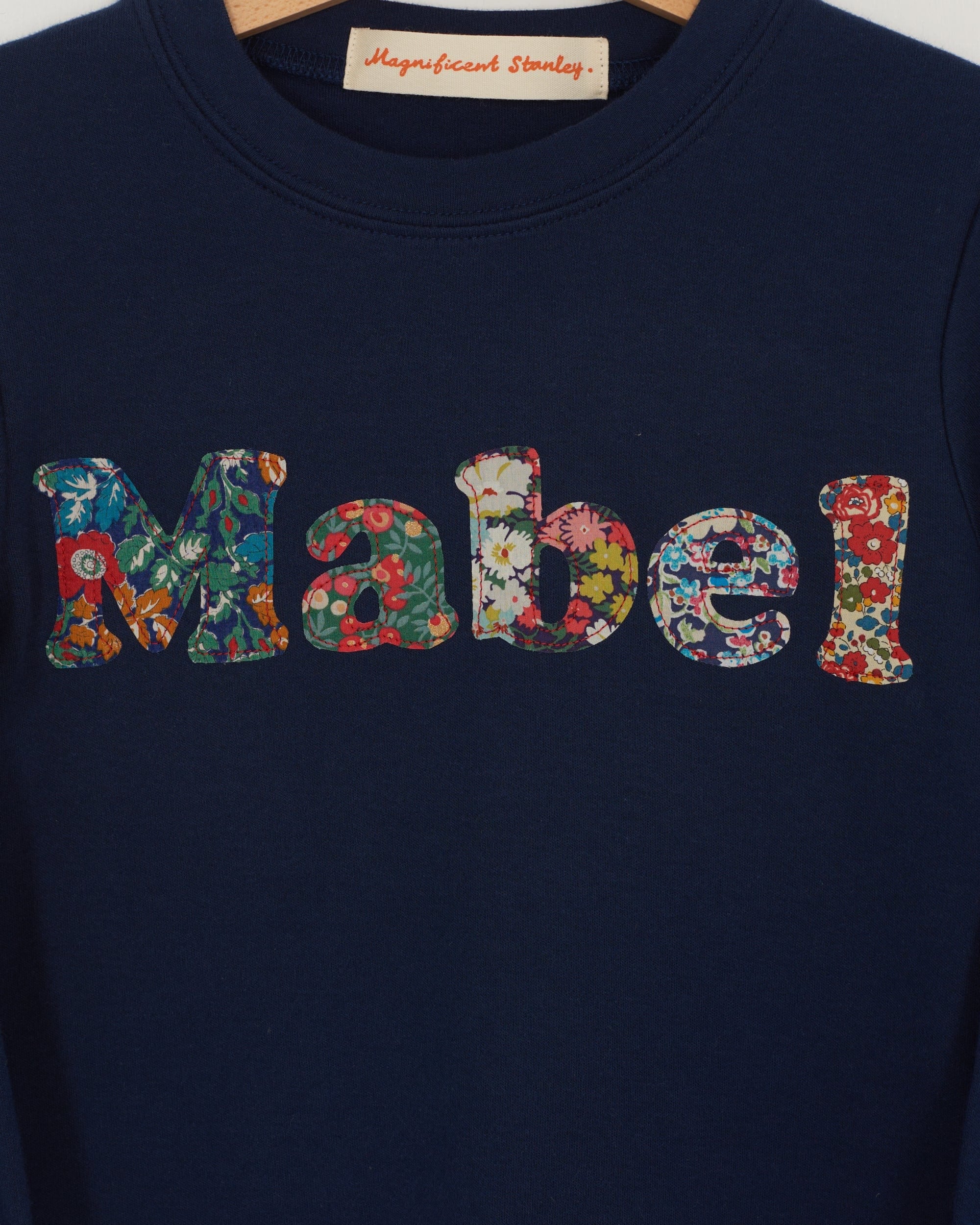 A navy t-shirt with the name mabel  sewn on in mixed Liberty print lowercase letters.