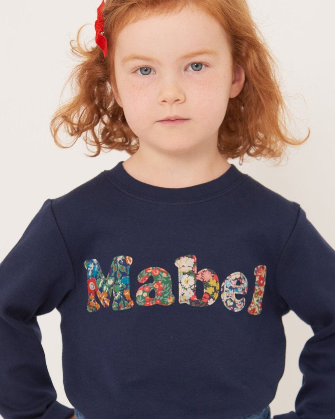 A 4 year old girl wearing a navy t-shirt with her name sewn on in mixed Liberty print lowercase letters.