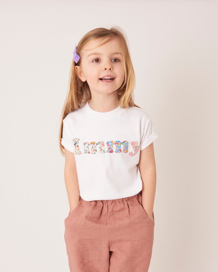A 5 year old girl wears a personalised white t-shirt with her name on in a mix of Liberty prints.