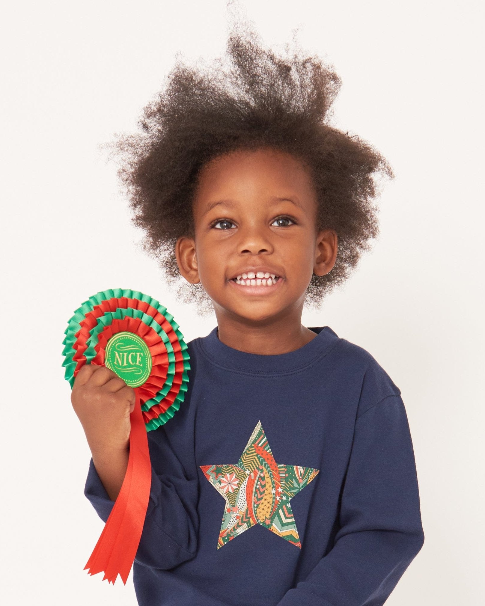 A 3 year old boy wearing a navy long sleeve christmas t-shirt with a festive star on the front made from Liberty My Little Star print on the front.
