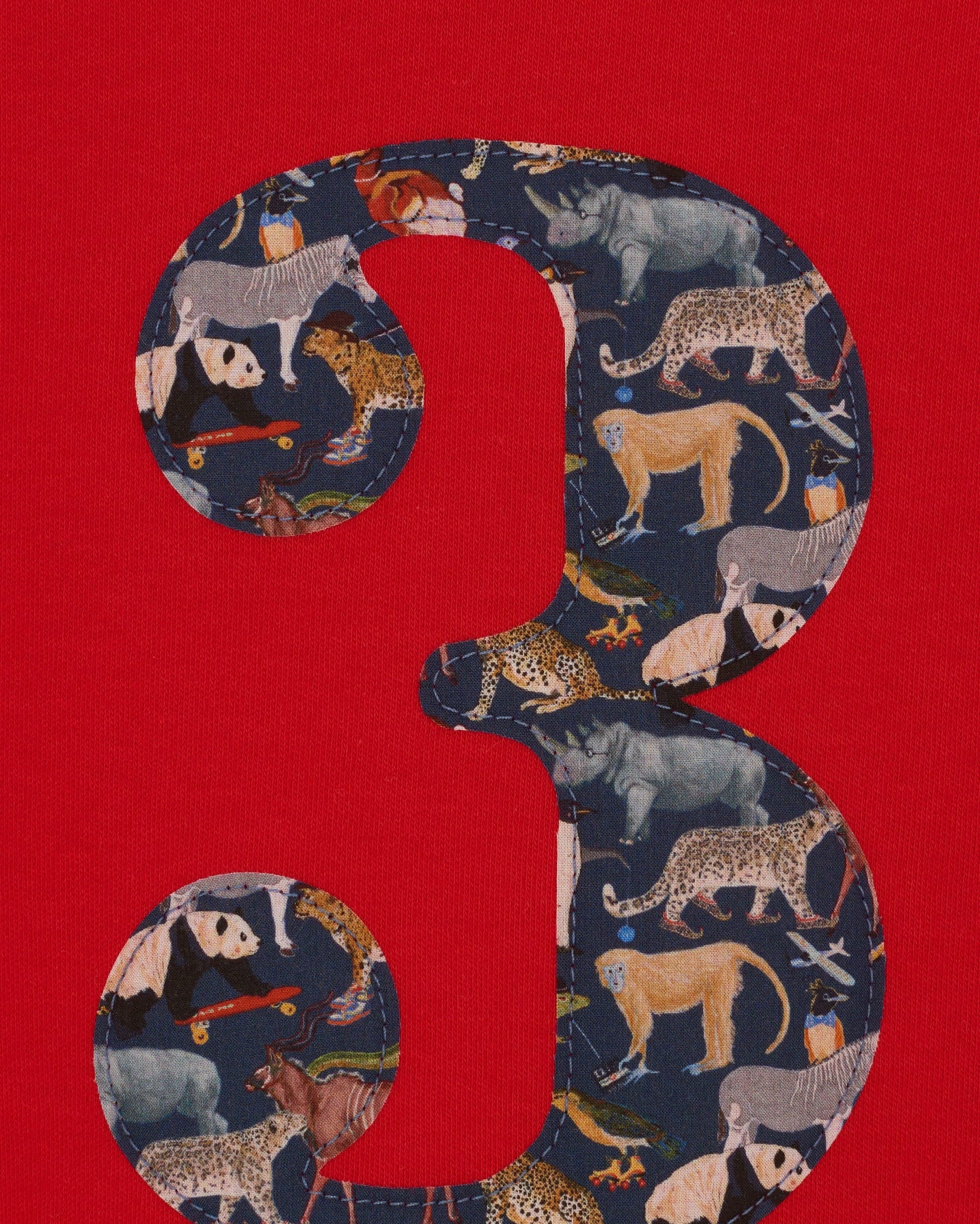 A close up of a red birthday t-shirt with a number 3 on the front made from Liberty zoo print fabric.