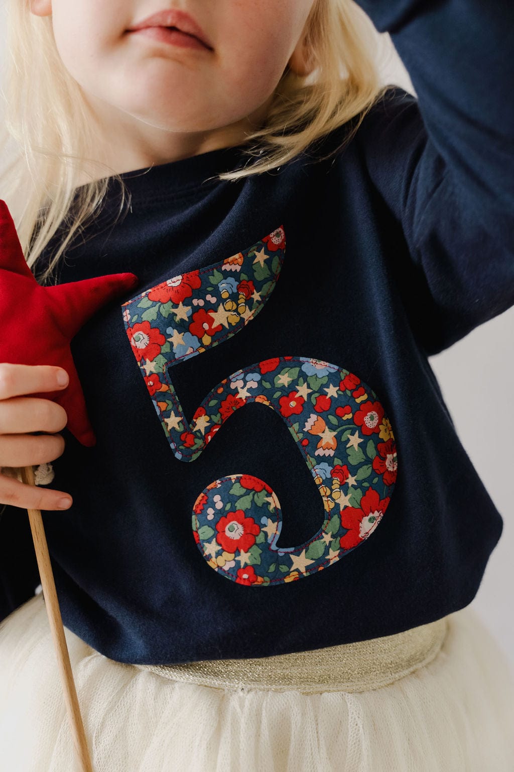 A girl wearing a navy t-shirt with a Liberty floral and star Betsy Star number 5 on the front.