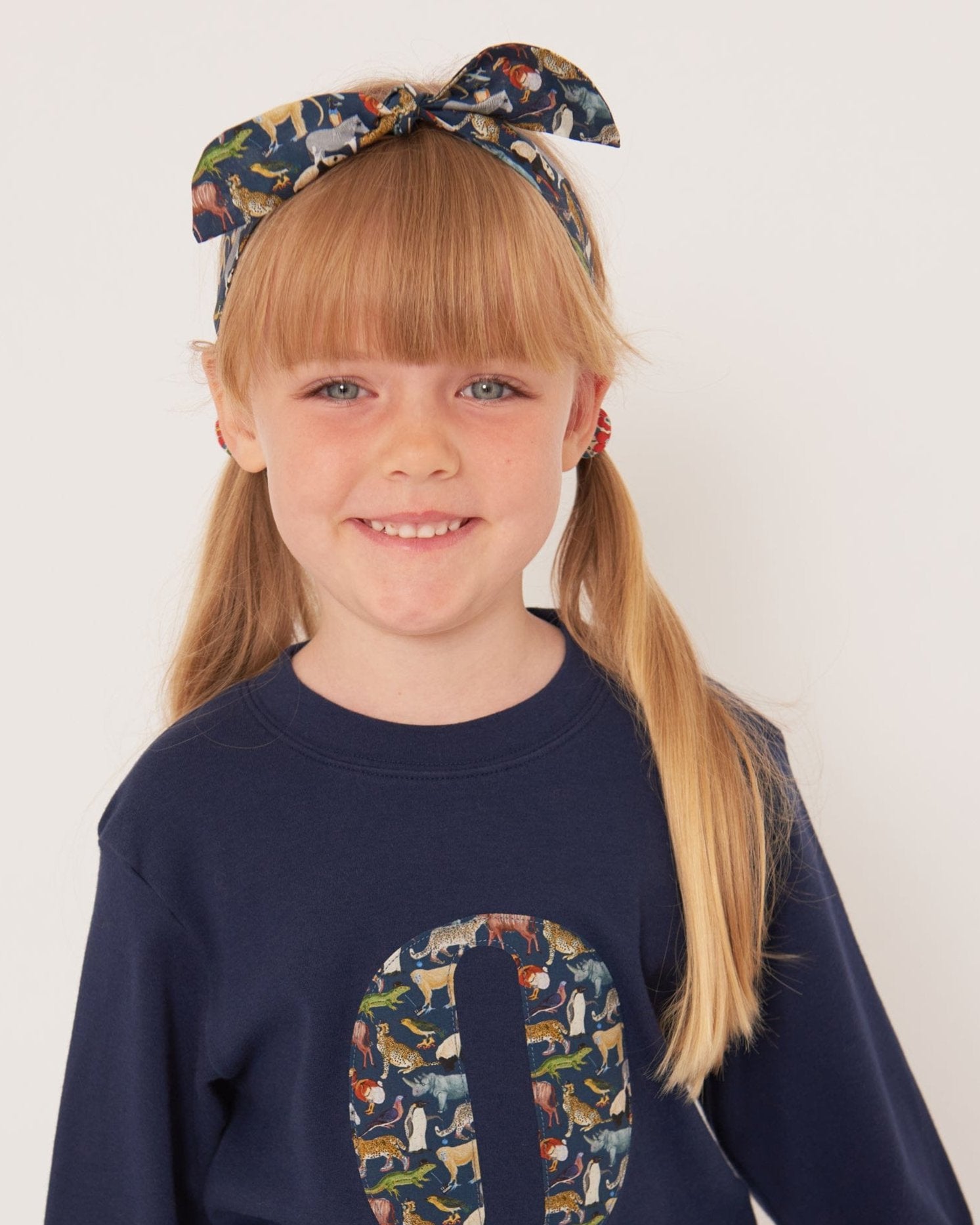 A smiling 5 year old girl wearing a personalised cotton navy long sleeve tee with her initial on the front made from Quey Zoo animal Liberty print fabric.