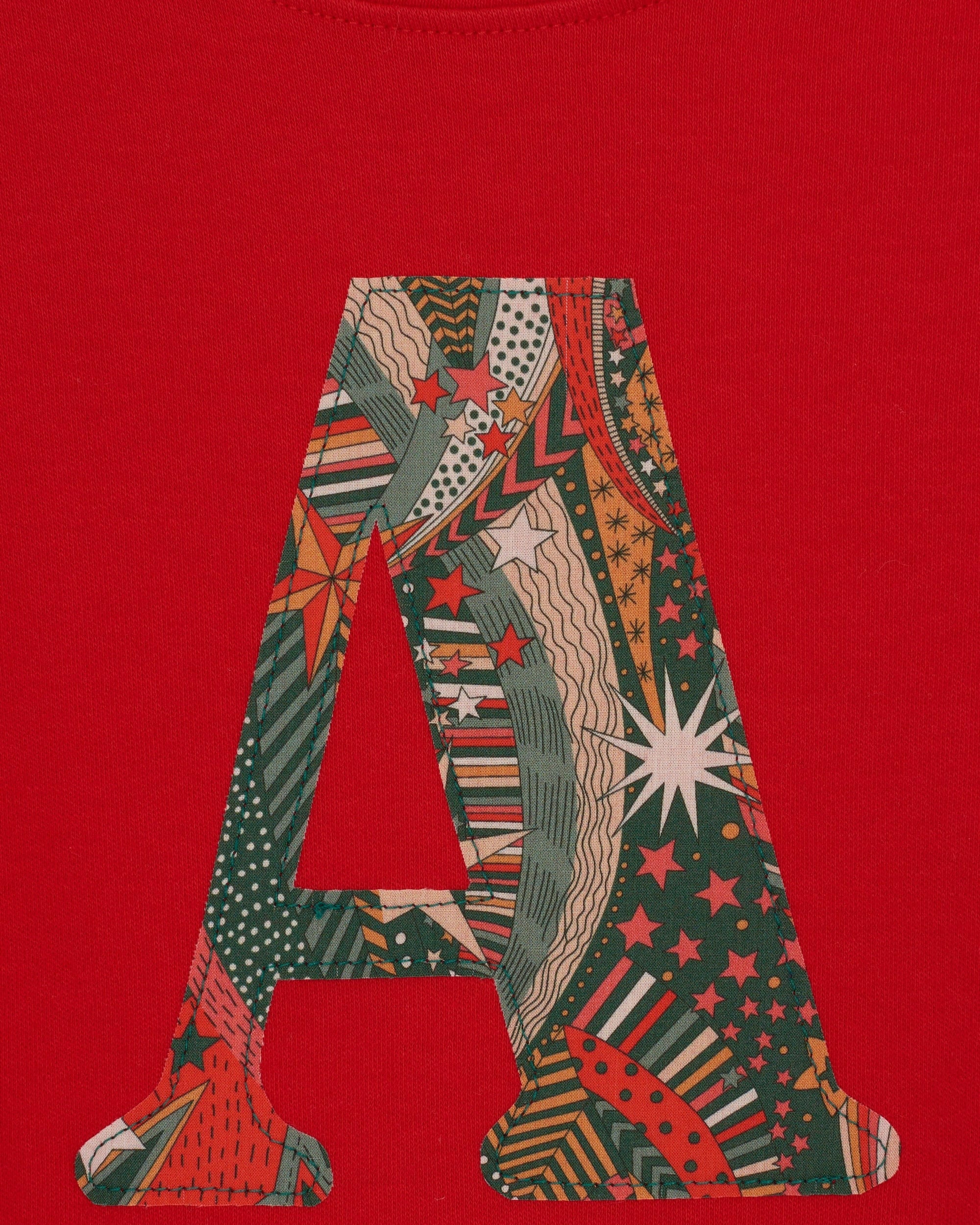 A close up of the appliqué on a personalised red cotton t-shirt with his initial in My Little Star Liberty print fabric.