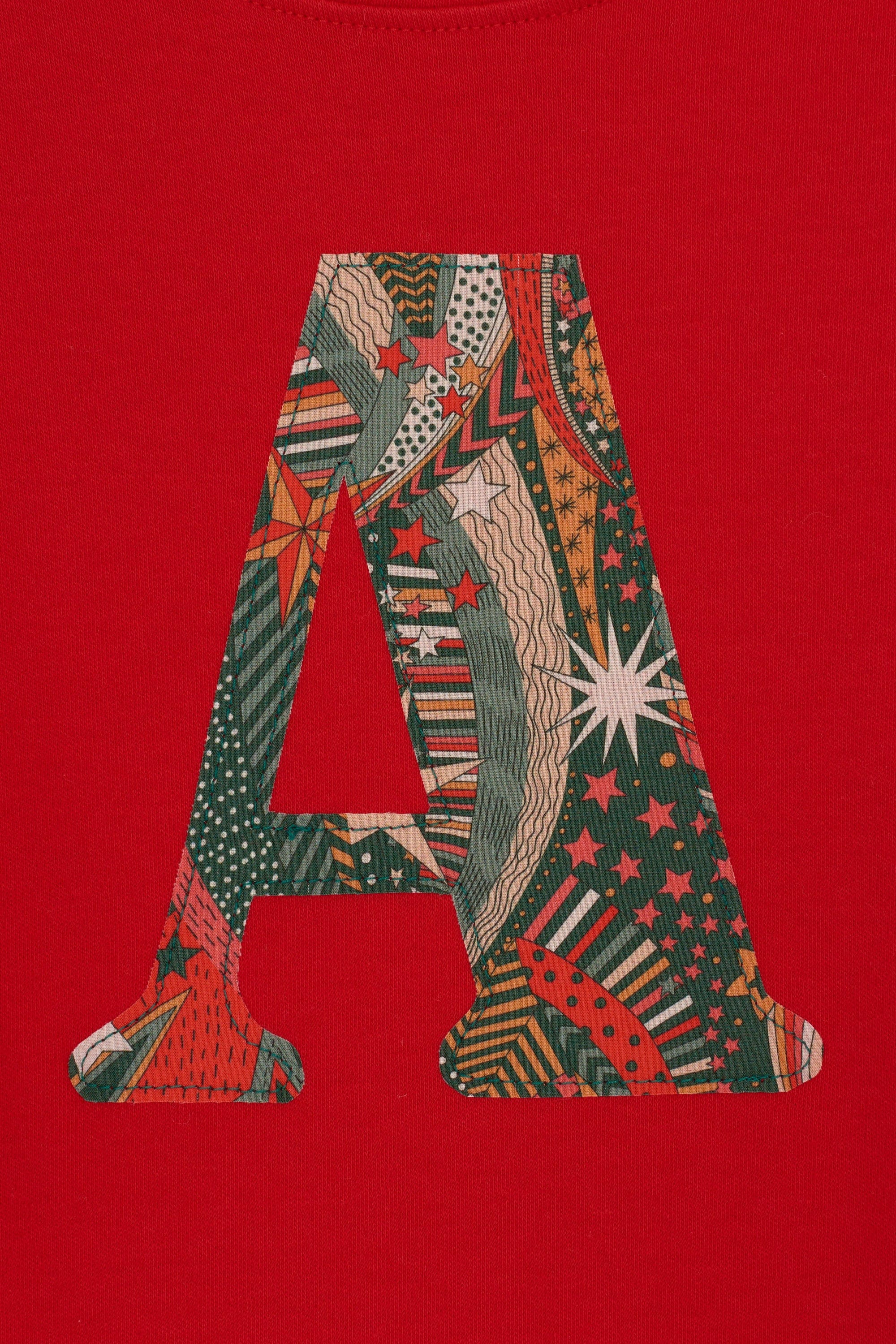 A close up of the appliqué on a personalised red cotton t-shirt with his initial in My Little Star Liberty print fabric.