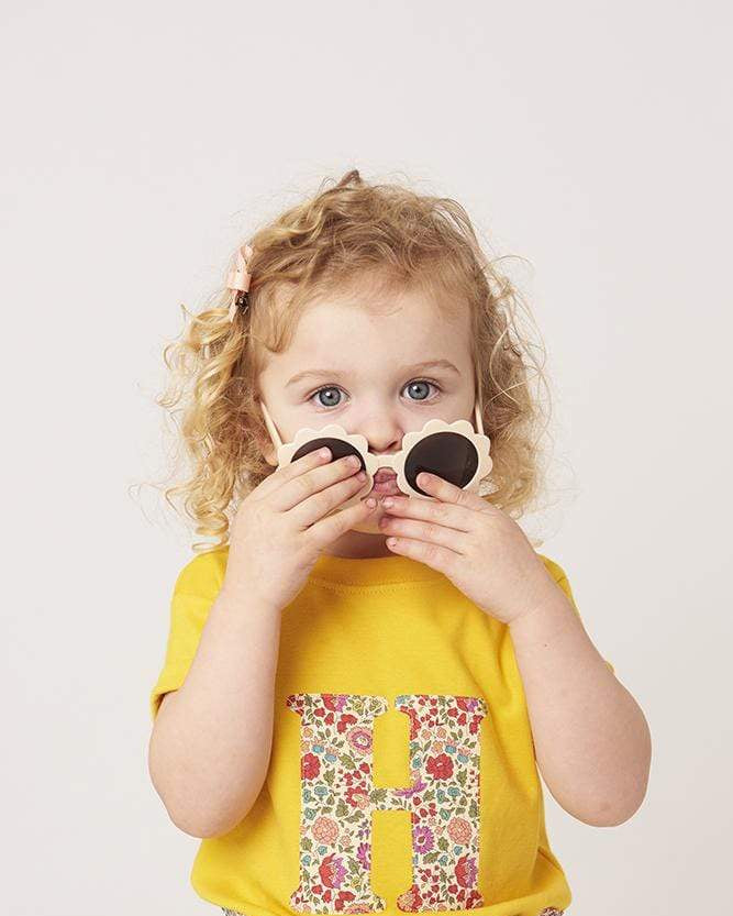 a smiling 2 year old girl wearing a personalised kids yellow t-shirt with an initial cut from d'anjo liberty floral print on the front