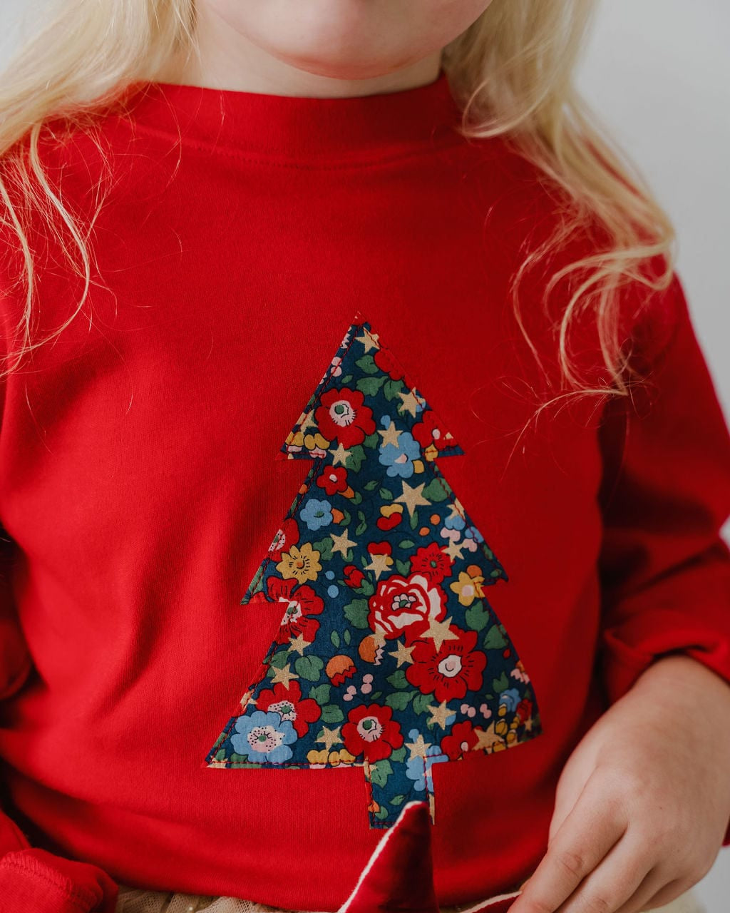 A 5 year old girl wearing a red Christmas t-shirt with a liberty floral Christmas tree appliquéd on the front.
