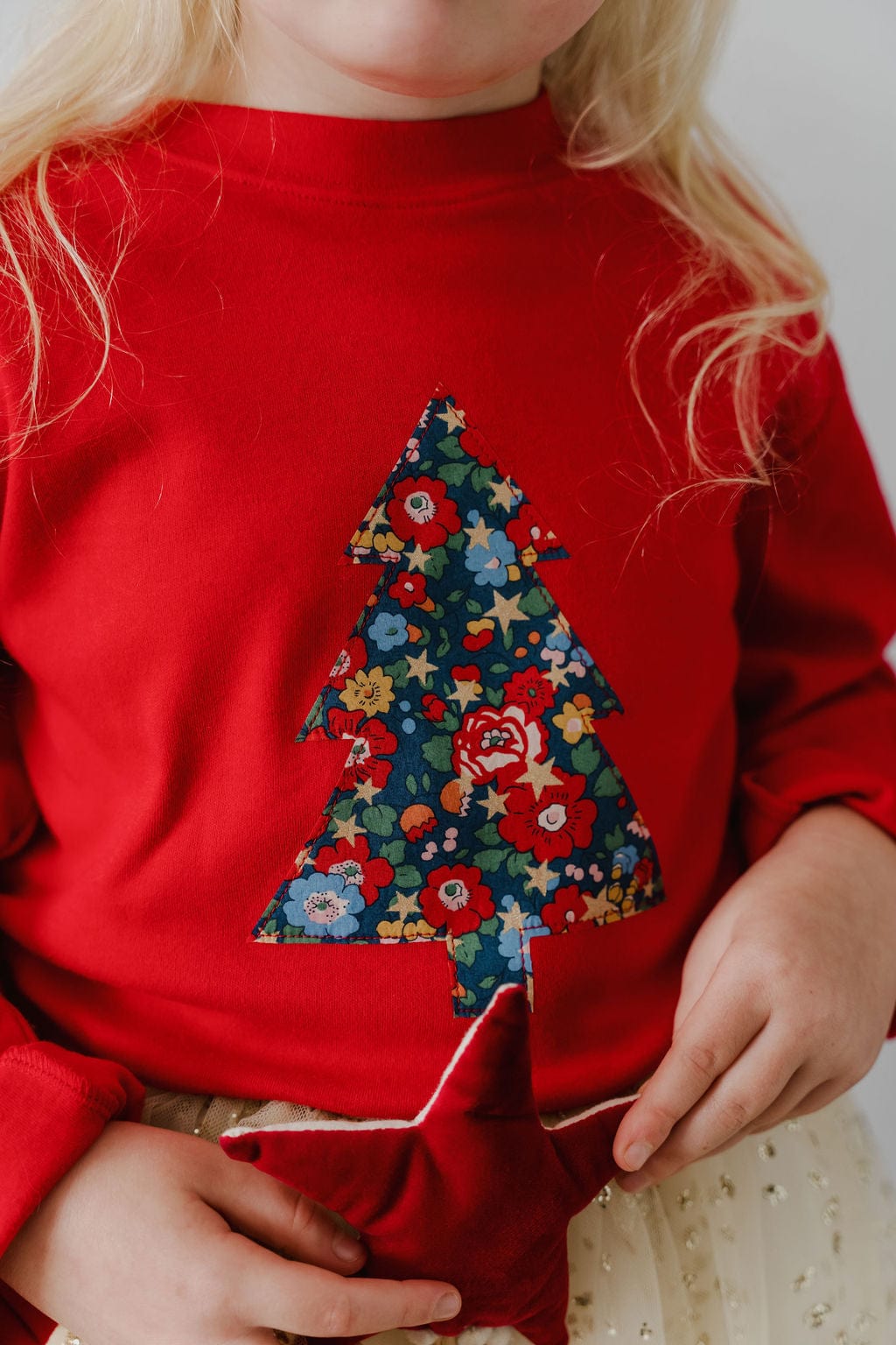 A 5 year old girl wearing a red Christmas t-shirt with a liberty floral Christmas tree appliquéd on the front.