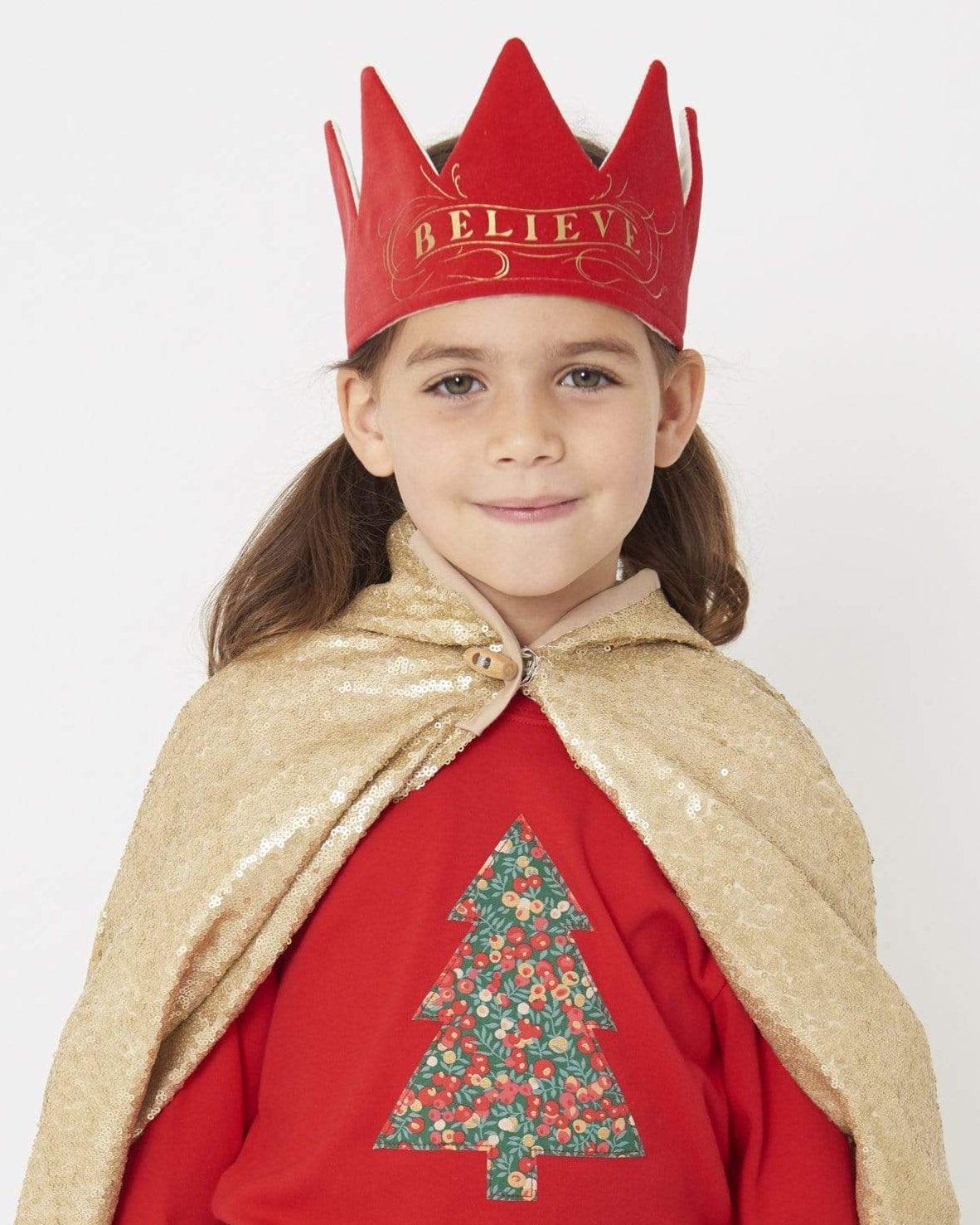 A smiling 5 year old girl wearing a festive red t-shirt with a Christmas tree on the front made from Liberty Glitter Wiltshire berry fabric.