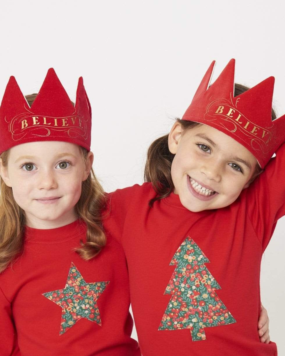 2 smiling 5 year old girls wearing festive red t-shirts with a star and Christmas tree on the front made from Liberty Glitter Wiltshire berry fabric.