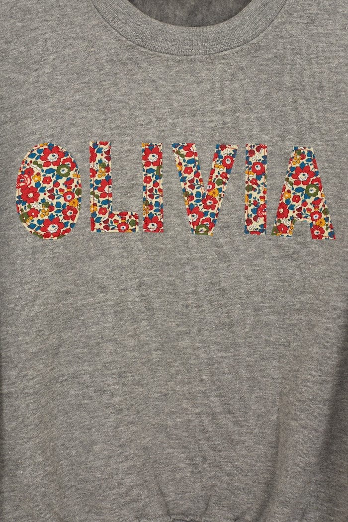 a grey kids personalised sweatshirt with the name Olivia on it cut from Betsy Ann Liberty print.