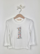 White long-sleeve shirt with a colourful Liberty betsy grey number '1' on a hanger against a white background