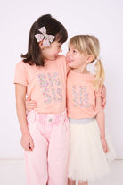 A girl wearing a BIG SIS pale Pink T-Shirt in Choice of Liberty Print as a proud big sister and a little sister wearing a 'lil sis' tee