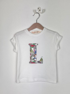 White t-shirt with colorful dinosaur Liberty print 'L' design on a hanger against a white background