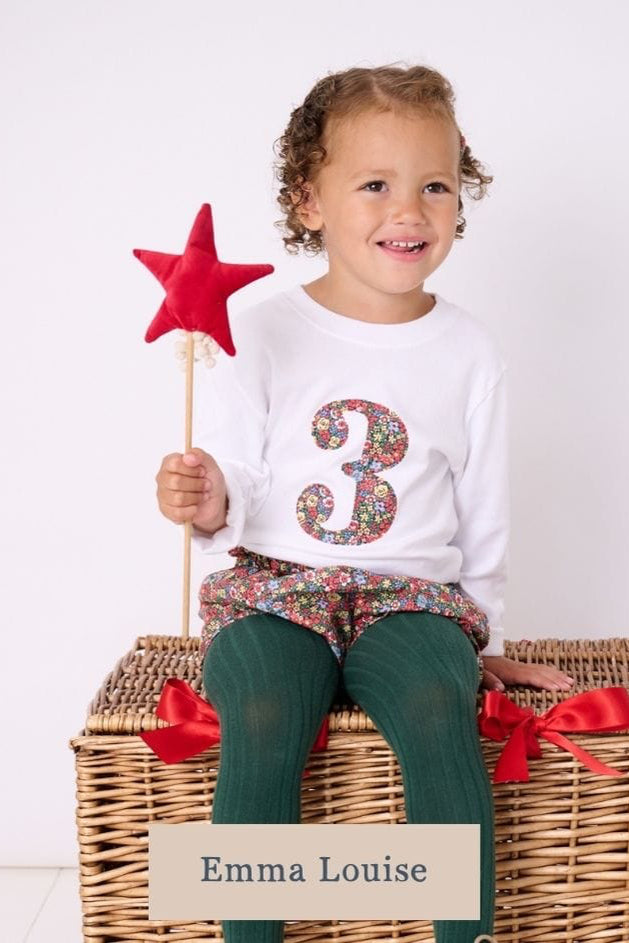 a little girl wearing a white birthday t-shirt with a number 3 cut from liberty floral print on the front
